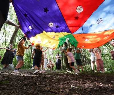 Lots of children playing under a multicoloured parachute.