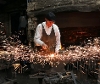 Blacksmith hitting a piece of metal with sparks flying across a workshop.
