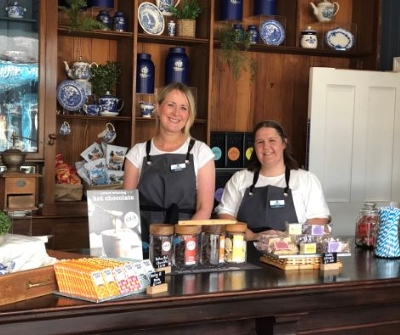 Two women behind the counter of the Victorian team room surrounded by chocolate bars and cakes available to eat.