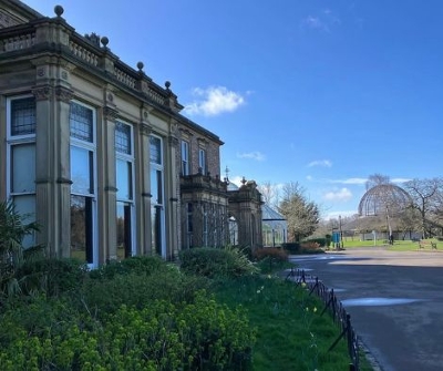 Old building surrounded by greenery and flowers with a blue sky and small puddles on the floor.