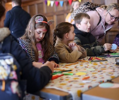3 children doing arts and crafts with 2 adults and one girl's face painted.