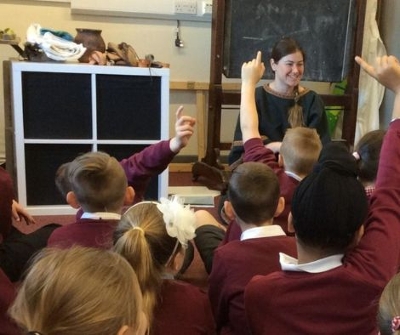 Classroom full of young students raising their hands to ask questions about historic items.