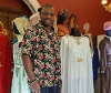 Man stood next to white dress with a collection of dresses around him.
