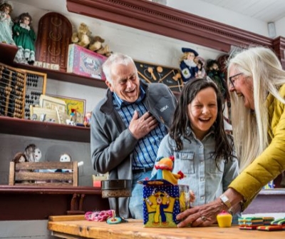 2 adults and a child playing with an old jack in the box toy surrounded by other old vintage toys.
