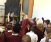 Classroom full of young students raising their hands to ask questions about historic items.