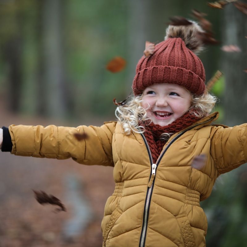 Young Girl Throwing Autumn Leaves In The Air In The Park