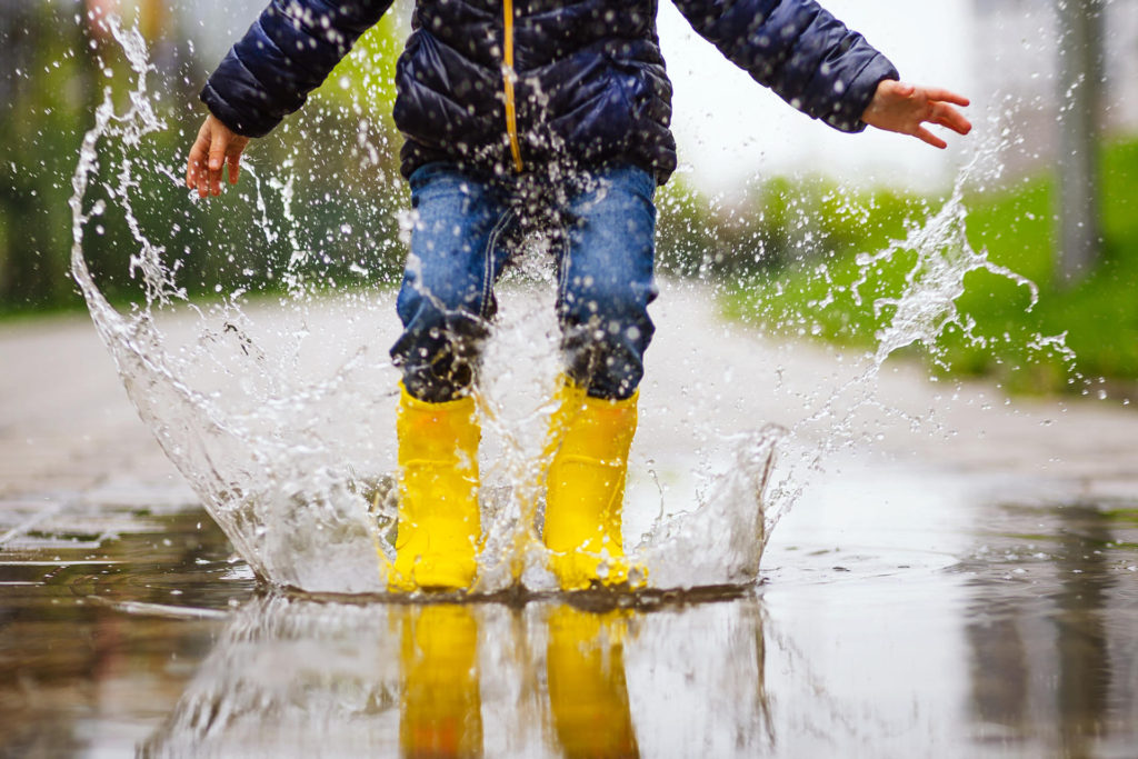 Child Jumping In Puddle On Autumn Walk