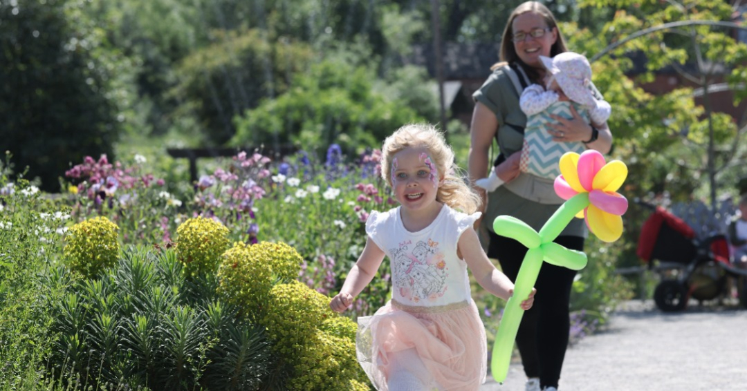 Girl running in Walled Garden with flower balloon - 70th ann